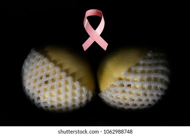 two yellow pears in white shells, similar to a bra with a pink ribbon in the middle above them, symbolizing the fight against cancer. Isolated on the black background
