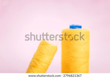 Two yellow thread spools with blue caps on soft background, sewi