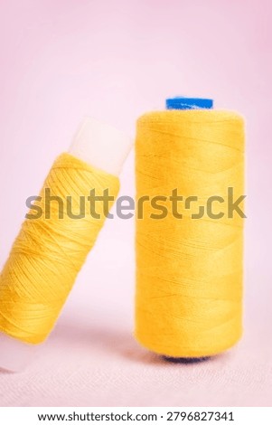 Two yellow thread spools with blue caps on soft background, sewi