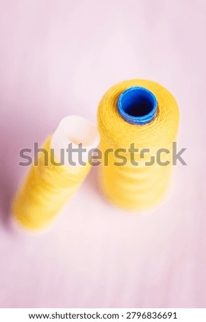 Two yellow thread spools with blue caps on soft background, sewi