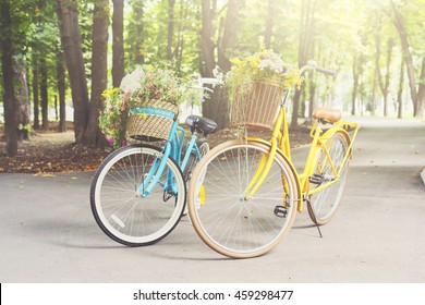 Two yellow and turqoise city woman bikes with flowers in park. Bright lady bicycles vintage style with baskets full of wildflowers in summer sunny town. Elegant recreational vehicles
