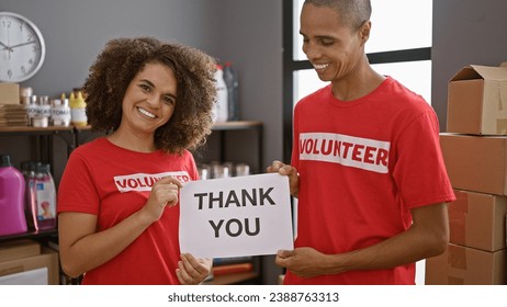 Two young activists, smiling man and woman volunteers holding a 'thank you' message at charity center, uniting community with their altruism and dedication - Powered by Shutterstock