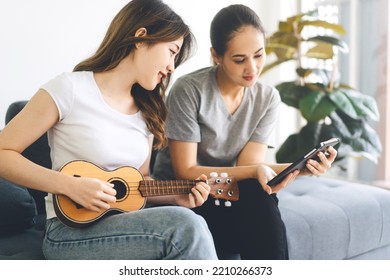 Two Young Adult Woman Living Together With Relationship Concept. Southeast Asian People Couple Relax Lifestyle Playing Music On Sofa Life Moments At Home.