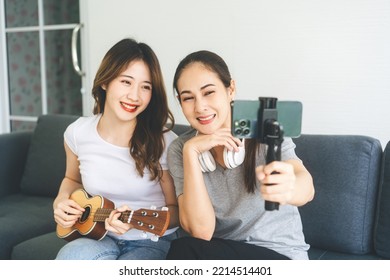 Two Young Adult Woman Living Together With Relationship Concept. Southeast Asian People Couple Relax Lifestyle Playing Music On Sofa Life Moments At Home.