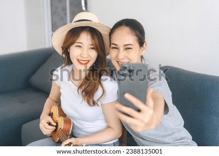 Two young adult woman living together with relationship concept. Southeast asian people couple relax lifestyle playing music on sofa life moments at home.