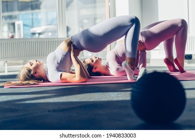 Two Young Adult Women Doing Pelvic Muscle Exercises On Separate Rectangular Mats With Weights And Stability Ball In The Foreground In The Fitness Studio. Toned