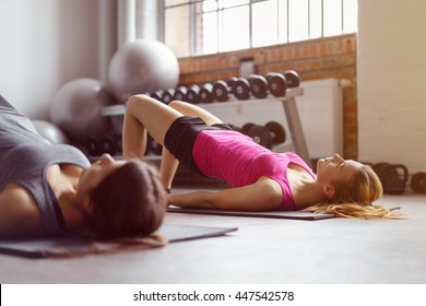 Two Young Adult Women Doing Pelvic Muscle Exercises On Individual Rectangular Mats With Weights And Stability Ball In Background At Gym