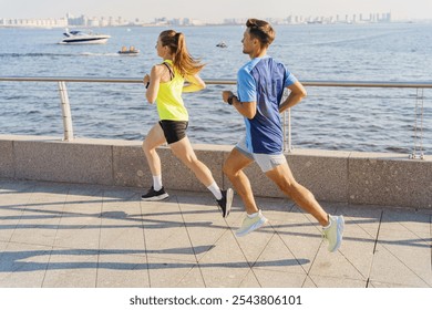 Two Young Adults Jogging Along a Waterfront Promenade Under a Clear Sky in the Afternoon Light - Powered by Shutterstock