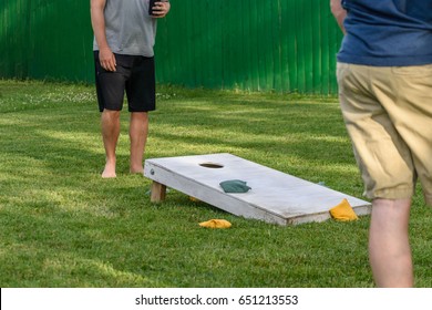 two young adults playing bags game in backyard on sunny summer day - soft focus