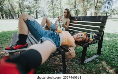 Two young adults relax on a park bench, enjoying a sunny day with refreshing drinks and playful smiles. - Powered by Shutterstock