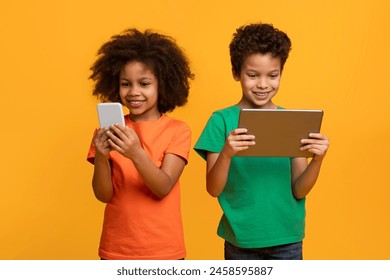 Two young African American children, possibly siblings or friends, are standing next to each other holding a tablet and cell phone - Powered by Shutterstock