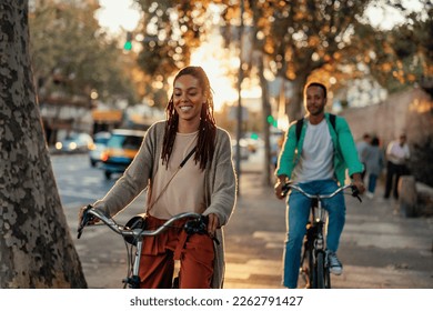 Two young African American people are outside in the city riding their bicycles on a beautiful sunny day.