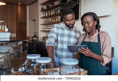 Two young African entrepreneurs working together on a digital tablet at the checkout counter of their trendy cafe  - Powered by Shutterstock