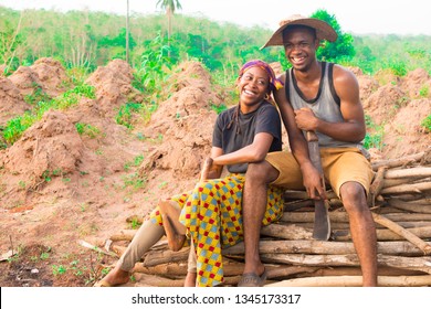 Two Young African Farmers Sitting On A Pile Of Wood On A Farm Laughing Together