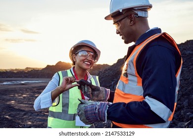 Two young African mine workers wearing protective wear are discussing coal quality while on site at a coal mine