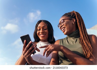 two young african women having fun looking at the cell phone, concept of youth and communication technology, copy space for text - Shutterstock ID 2118343373