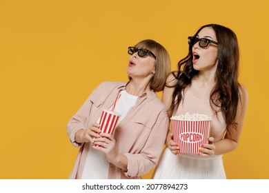Two young amazed daughter mother woman in 3d glasses watch movie film hold bucket of popcorn cup of soda pop isolated on yellow background studio portrait People emotions in cinema lifestyle concept