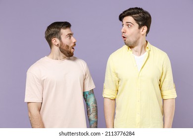 Two Young Amazed Shocked Men Friends Together In Casual T-shirt Tattoo Translate Fun Look To Each Other With Open Mouth Isolated On Purple Color Background Studio Portrait People Lifestyle Concept.