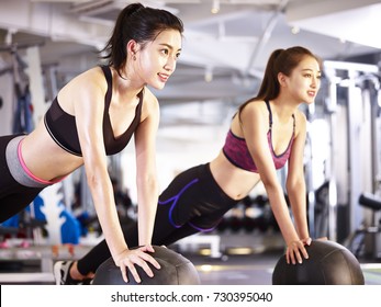 Two Young Asian Adult Women Working Out In Gym Using Medicine Balls.