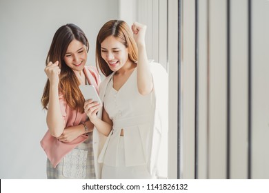 Two Young Asian Business Woman In Suit Using Smart Phone For Online Shopping, Internet Banking And Buying Service From The Internet.