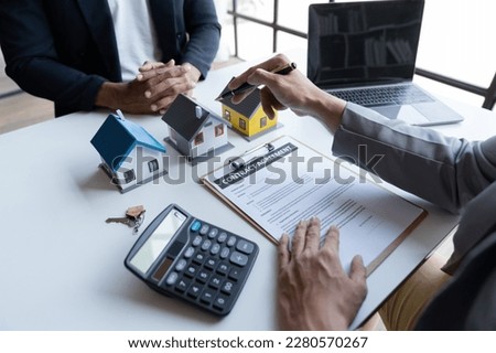 Two young Asian businessmen or architects are describing architectural house model in their office together for the construction of  housing estate project in  prime location the location is perfect