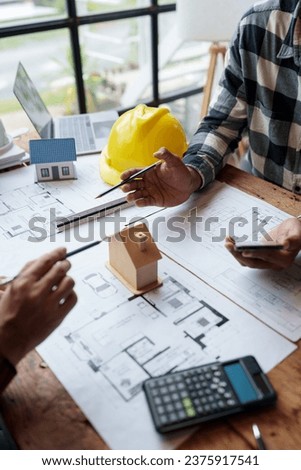 Two young Asian businessmen or architects are describing architectural house model in their office together for the construction of housing estate project in prime location the location is perfect