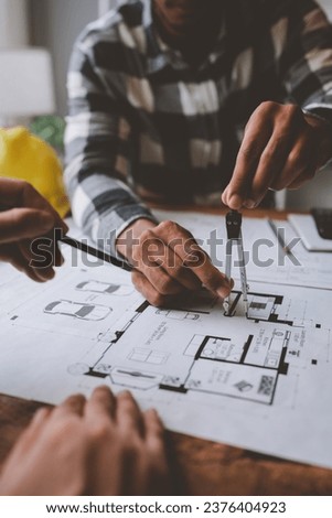 Two young Asian businessmen or architects are describing architectural house model in their office together for the construction of housing estate project in prime location the location is perfect