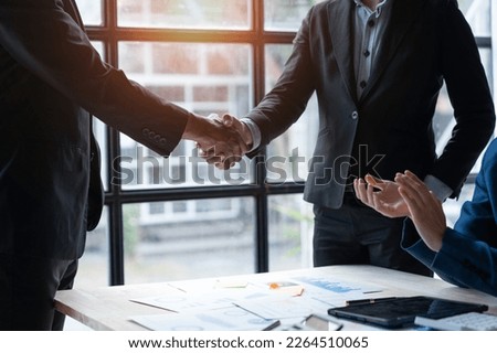 Two young Asian businessmen shaking hands and agreeing to invest in a real estate joint venture at the office.
