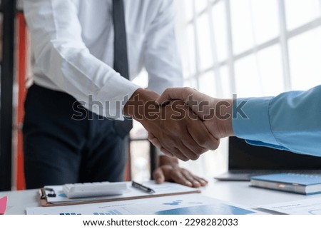 Two young Asian businessmen shaking hands and agreeing to invest in a real estate joint venture at the office.