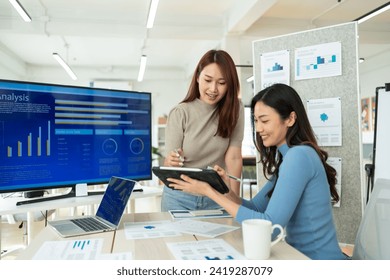 Two Young Asian businesswoman discuss with new startup project Idea presentation,analyze planning.Two cheerful diverse office workers women cooperating on project,looking at screen,paper sheet,smiling - Powered by Shutterstock