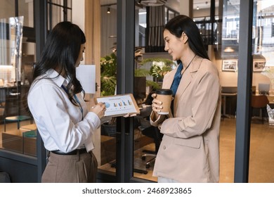 Two young Asian businesswomen discussing financial report on tablet during coffee break - Powered by Shutterstock