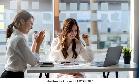 Two Young Asian Businesswomen Show Joyful Expression Of Success At Work Smiling Happily With A Laptop Computer In A Modern Office.