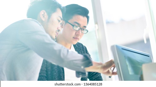 Two Young Asian Corporate Executives Working Together Using Desktop Computer.