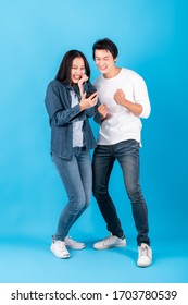 Two Of Young Asian Couple Man And Woman Using Mobile Phone With Happy And Cheerful Surprise Over Blue Background, Studio Shot Full Length