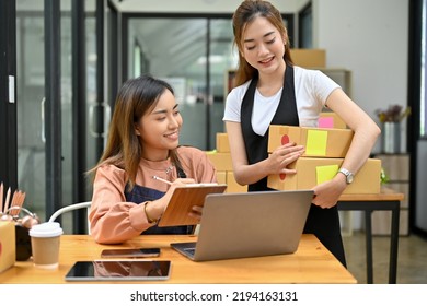 Two Young Asian Female Friends Online Shop Owner Working Together In The Stock Room, Preparing Shipping Boxes And Checking Orders.