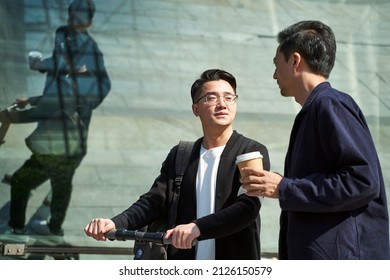 two young asian friends colleagues chatting while walking on street