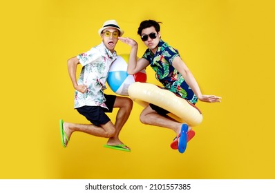 Two Young Asian Guys In Summer Casual With Hat And Sunglasses Jumping Up High With Funny Gesture With Beach Ball And Ring Float As Excited And Happy To Having Fun Playing At Swimming Pool On Vacation.