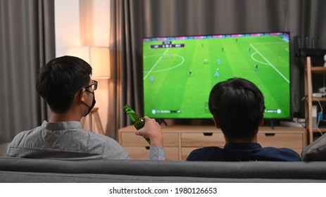 Two Young Asian Man Holding Glasses Of Beer And Cheering Football Match At Home.