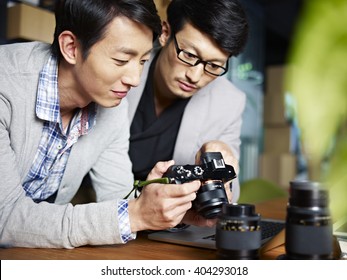 two young asian photographers designers checking pictures in camera in studio. - Powered by Shutterstock