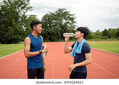 Two young Asian teenage athletes drinking water and resting during a break in track and field training, highlighting the importance of hydration - Powered by Shutterstock