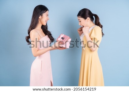 Two young Asian woman holding pink gift box on blue background