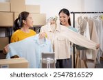 Two young asian woman live online clothing store while showing clothing with tablet on social at home, entrepreneur streaming for selling online clothing and presenting, online seller.