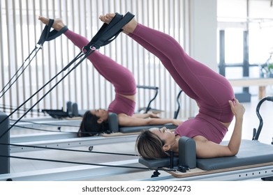 Two young asian women doing pilates exercises on a reformer.  - Powered by Shutterstock