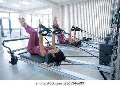 Two young asian women doing pilates exercises on a reformer.  - Shutterstock ID 2365346603