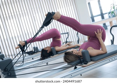 Two young asian women doing pilates exercises on a reformer.  - Powered by Shutterstock