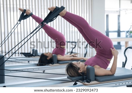Two young asian women doing pilates exercises on a reformer. 