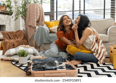 Two young asian women embrace and laugh together on a cozy couch, surrounded by moving boxes in a bright, well-lit living room. Happy Lesbian Couple Relaxing in Their New Home After Moving Day - Powered by Shutterstock