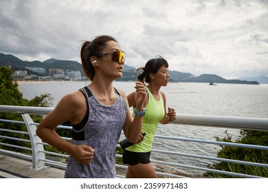 two young asian women female joggers exercising outdoors together in park by the sea - Powered by Shutterstock