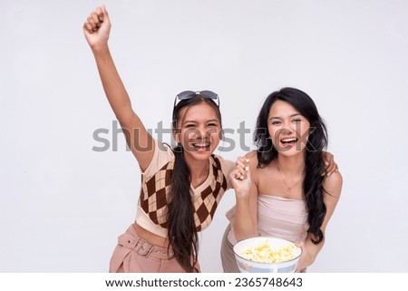 Two young asian women looking excited while eating popcorn together and cheering on their sports team on the tv. Isolated on a white background.