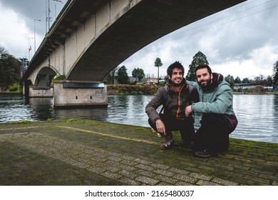 Two Young, Bearded, Happy And Handsome Brothers With Jacket And Backpack Eating Ceviche (fresh Raw Fish With Citrus Juice And Chili Peppers) And Panoramic View Of River, Bridge And Cloudy Sky,Valdivia